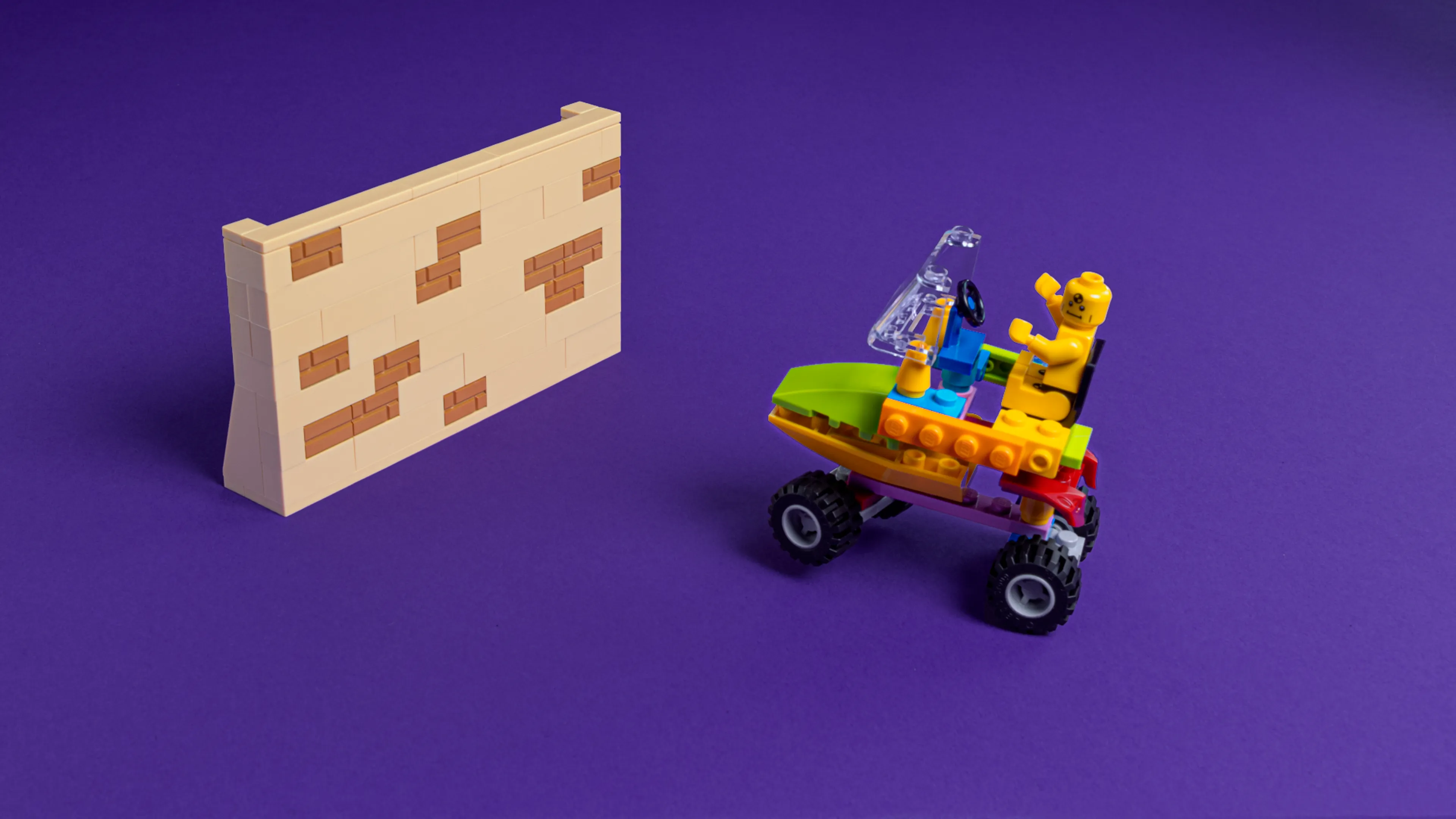 A LEGO vehicle heads towards a brick wall